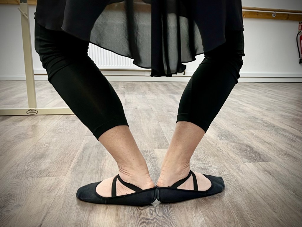 a dancer stands in a plié in first position the image shows her legs and feet